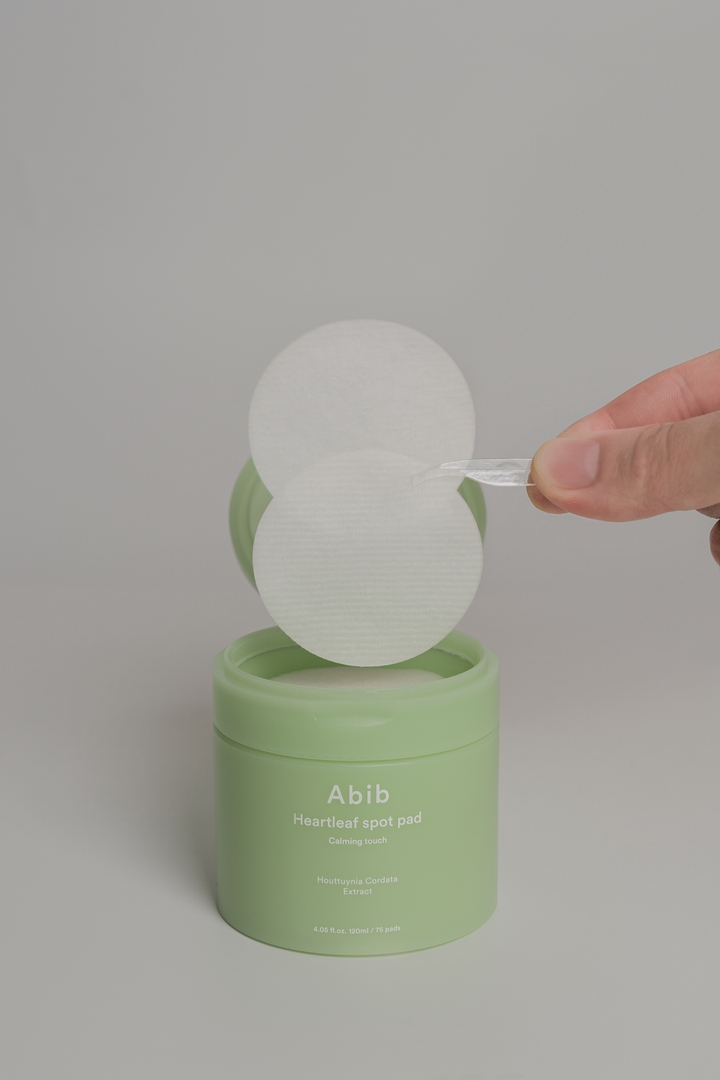 Abib Heartleaf Spot Pad Calming Touch 120ml 75 pads, peeling off a pad from the jar